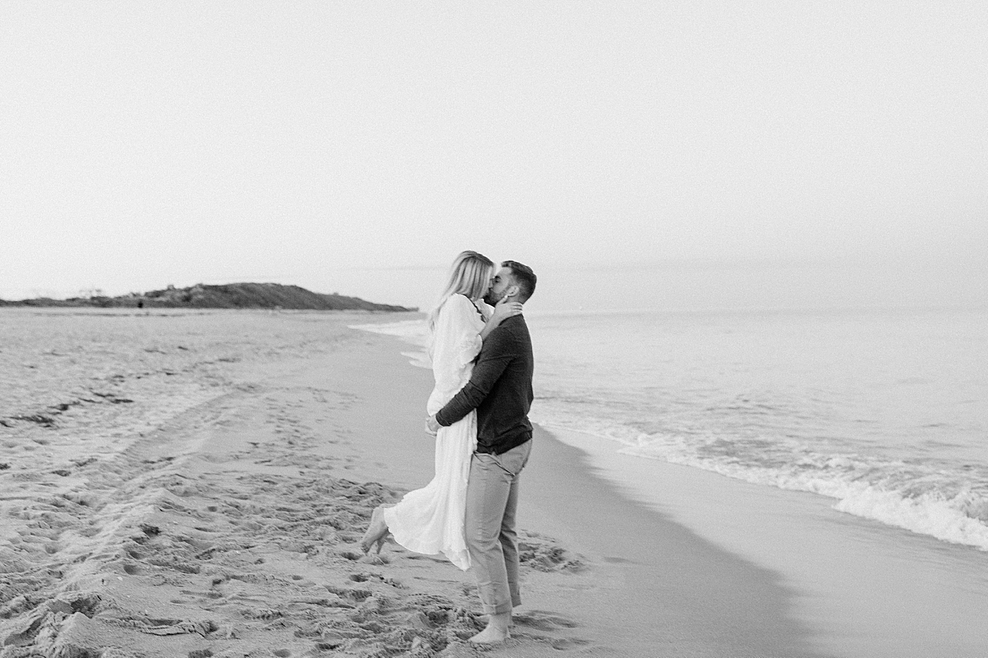 B&W man holding lady on the beach with calm ocean water Jupiter Engagement Photography captured by South Florida Engagement Photographer Erika Tuesta Photography
