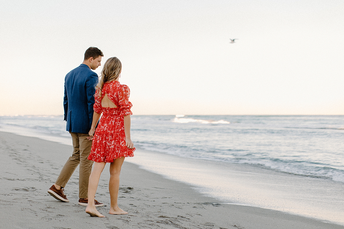 Couple holding hands strolling on the beach and looking at the calm ocean Red Reef Park Engagement Photography captured by South Florida Engagement Photographer