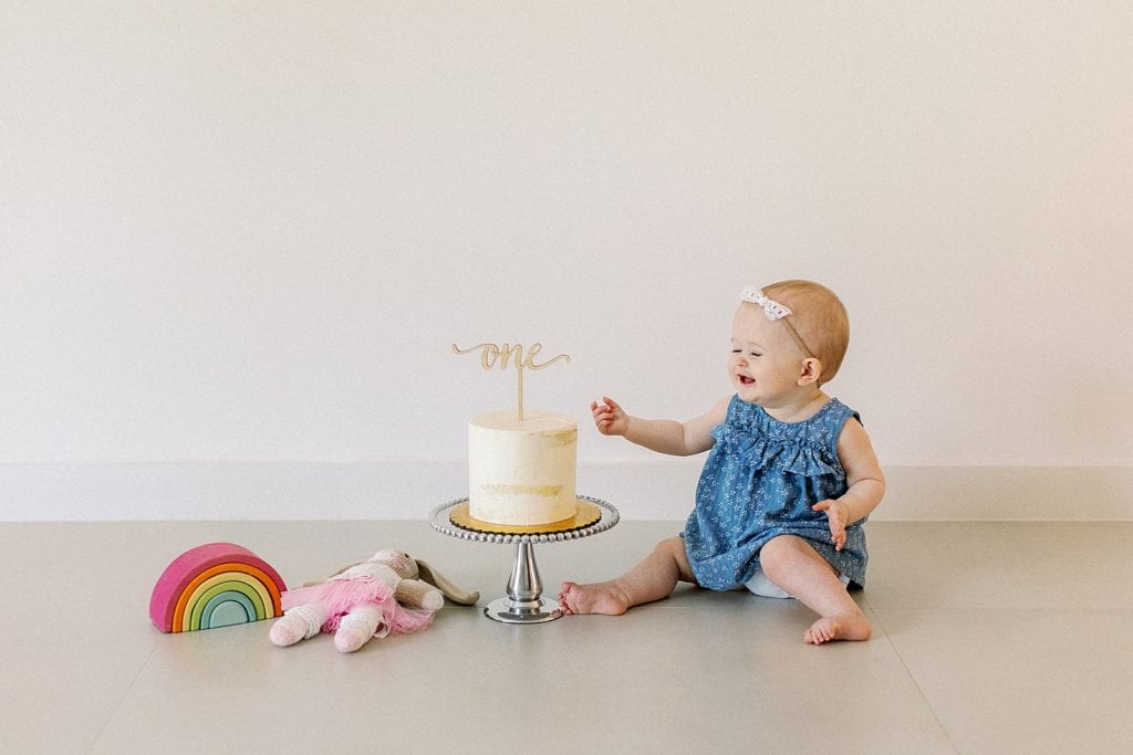 Baby girl sitting next to birthday cake