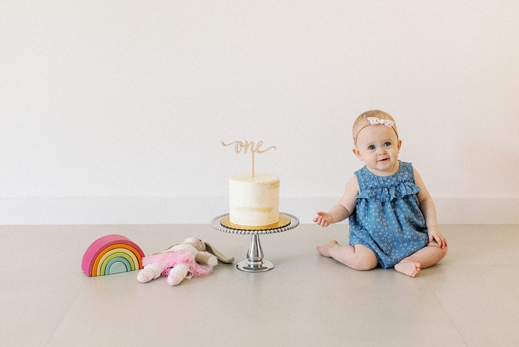 Baby girl sitting next to birthday cake