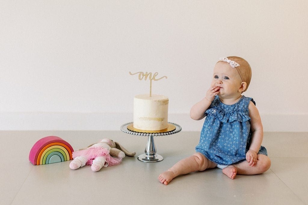 Baby girl sitting next to birthday cake and tasting a bite