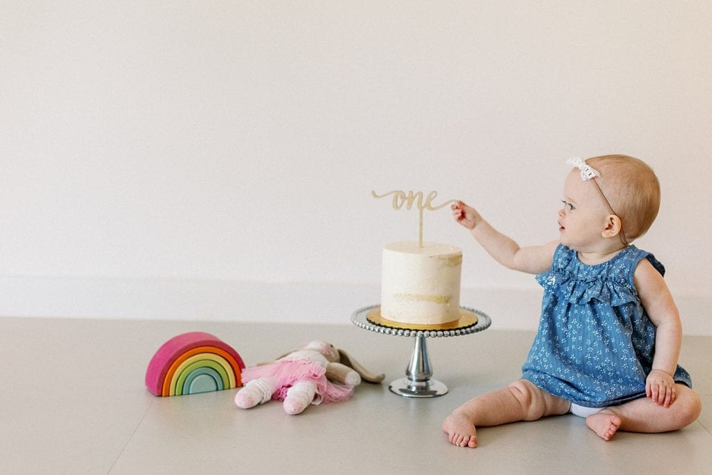 Baby girl sitting next to birthday cake playing with cake topper