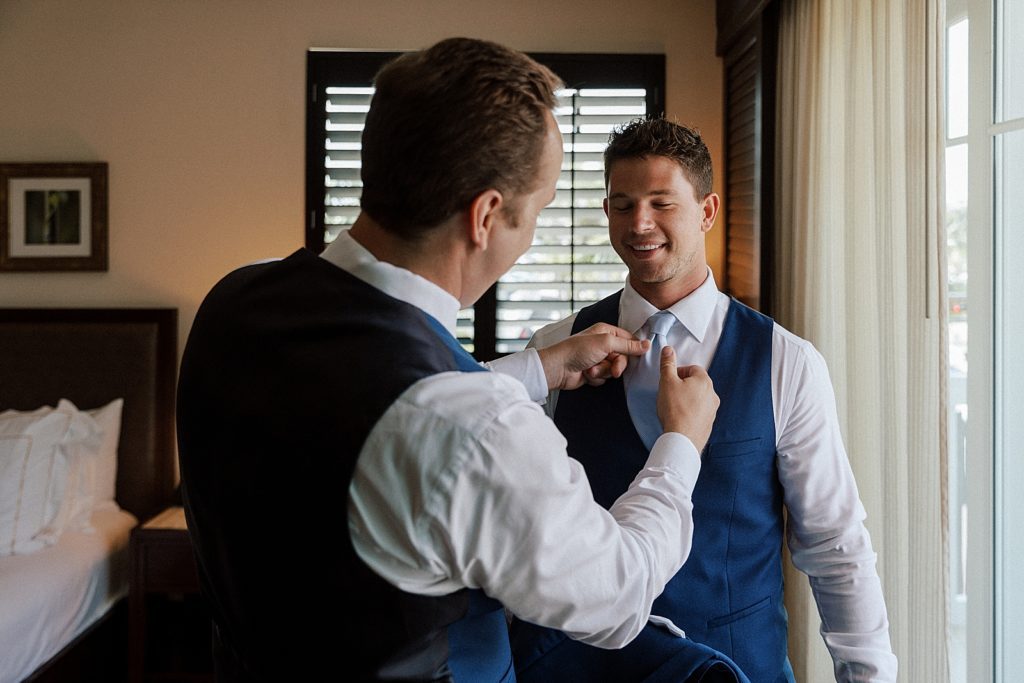 Groom getting help tying light blue tie from groomsman
