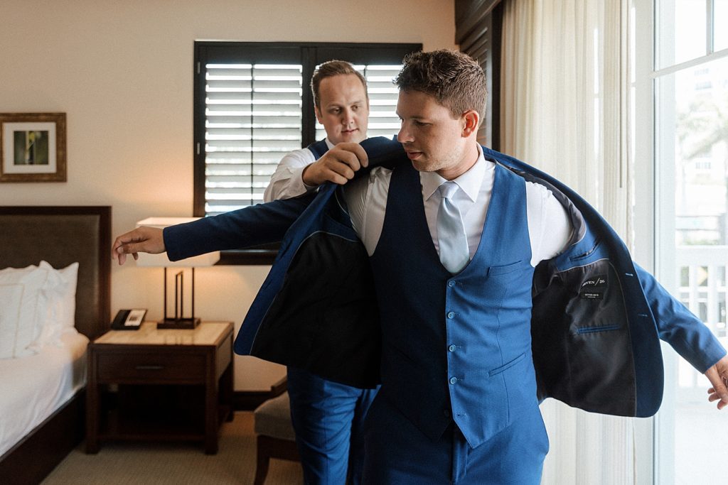 Groom getting ready with help from Groomsman to put on jacket