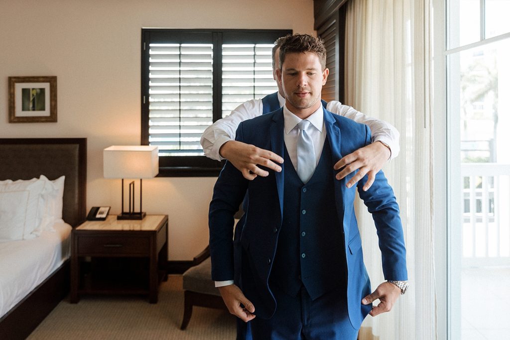 Groom getting ready with help from Groomsman to put on jacket