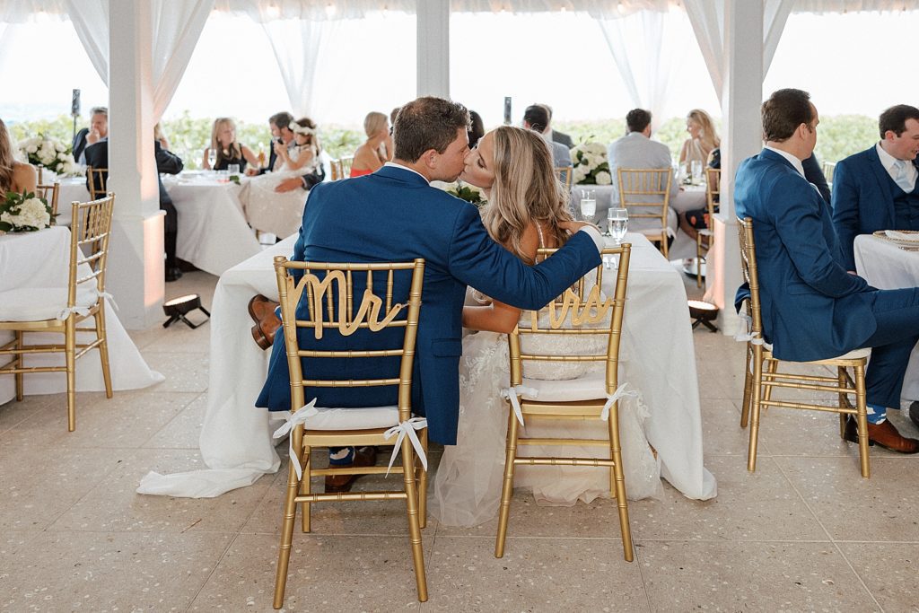 Bride and Groom kissing at sweetheart table with Mr and Mrs chairs