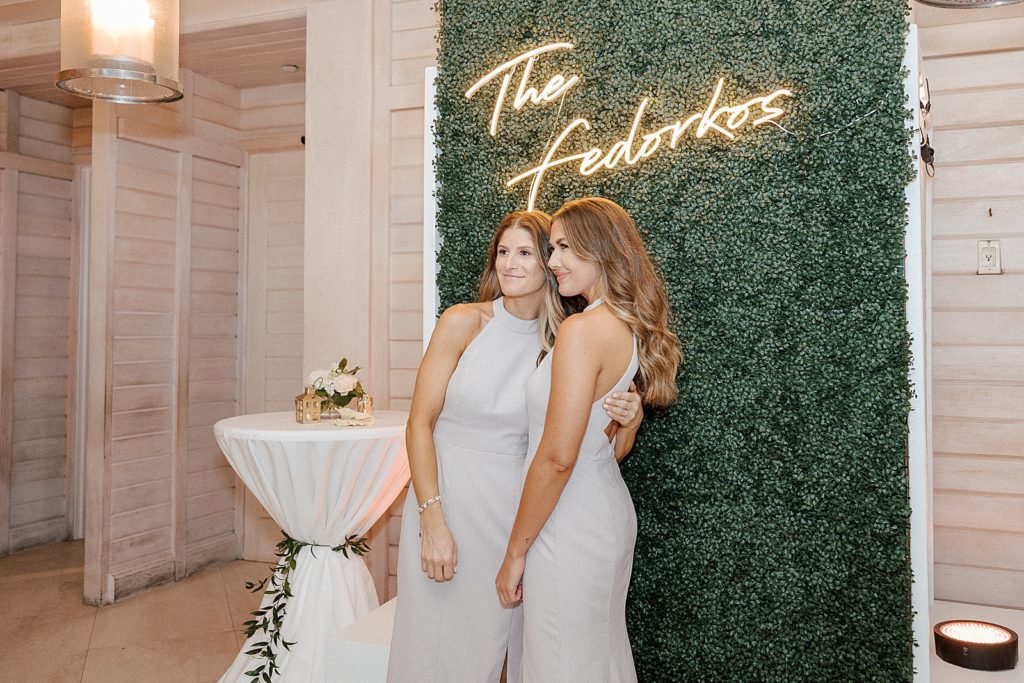 Bridesmaids posed by neon sign on greenery