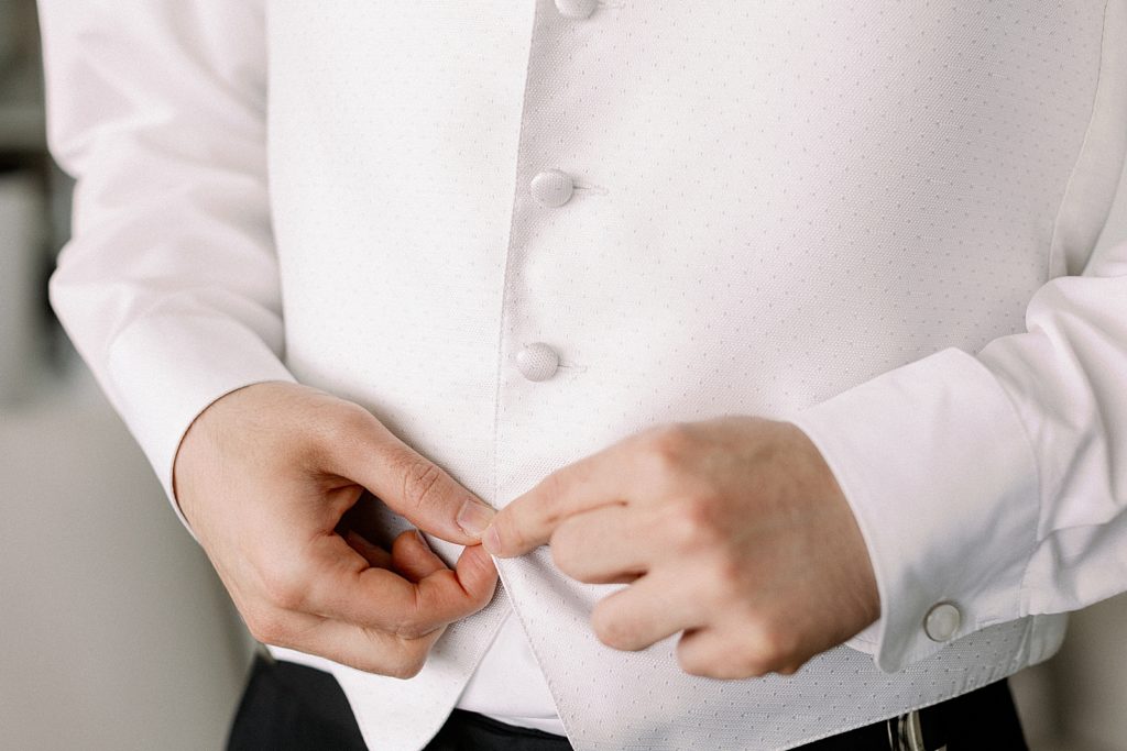 Closeup of Groom buttoning white vest