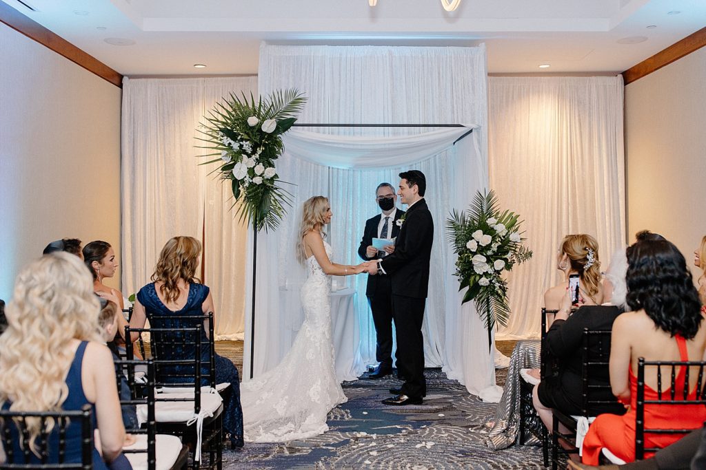 Bride and Groom hand in hand at the alter with indoor hotel Room