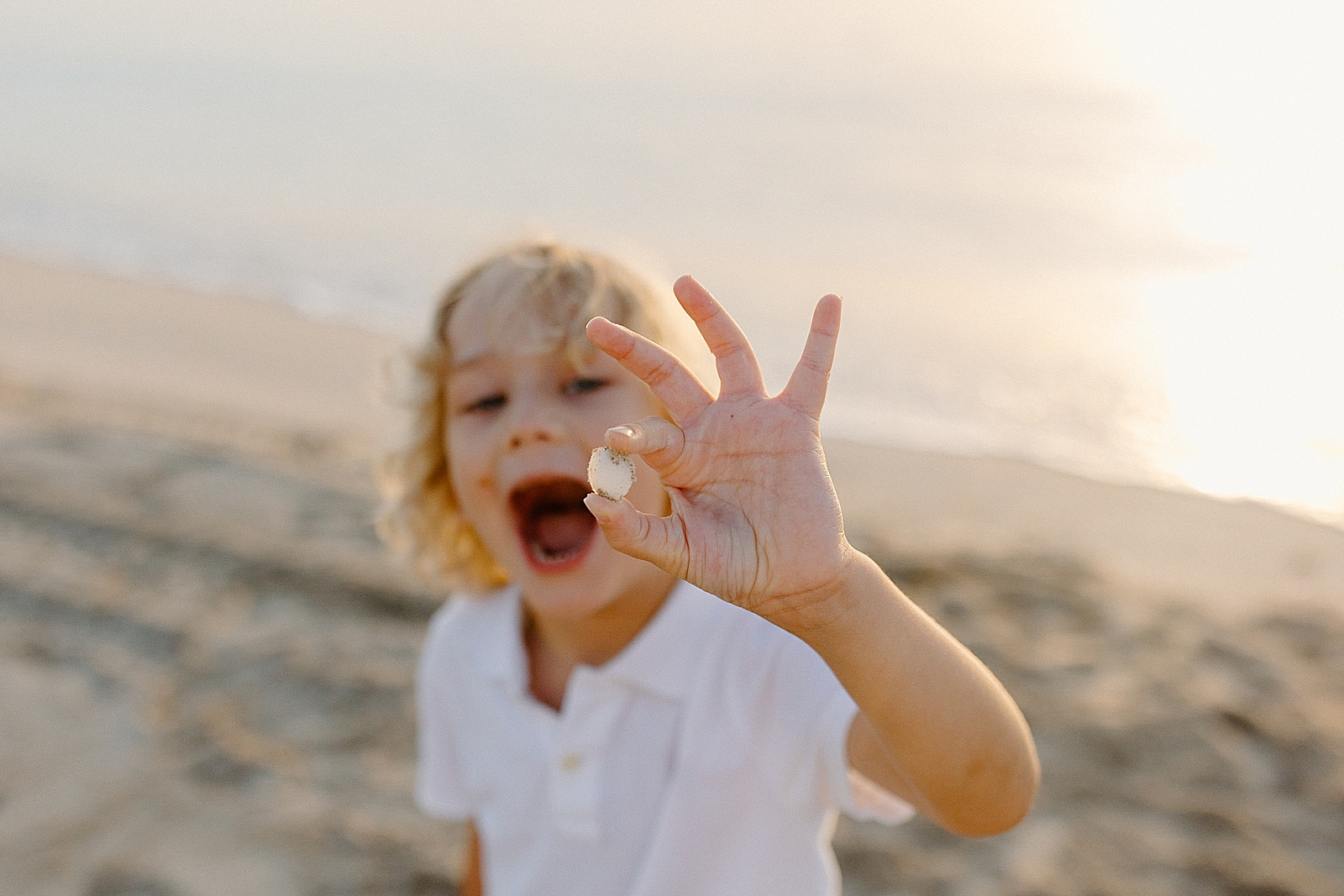 Boy holding seashell up and having mouth agape on the beach