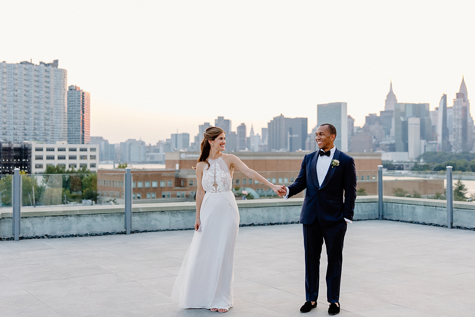 Bride and Groom extending and holding hands with East river Roosevelt Island and Empire State building