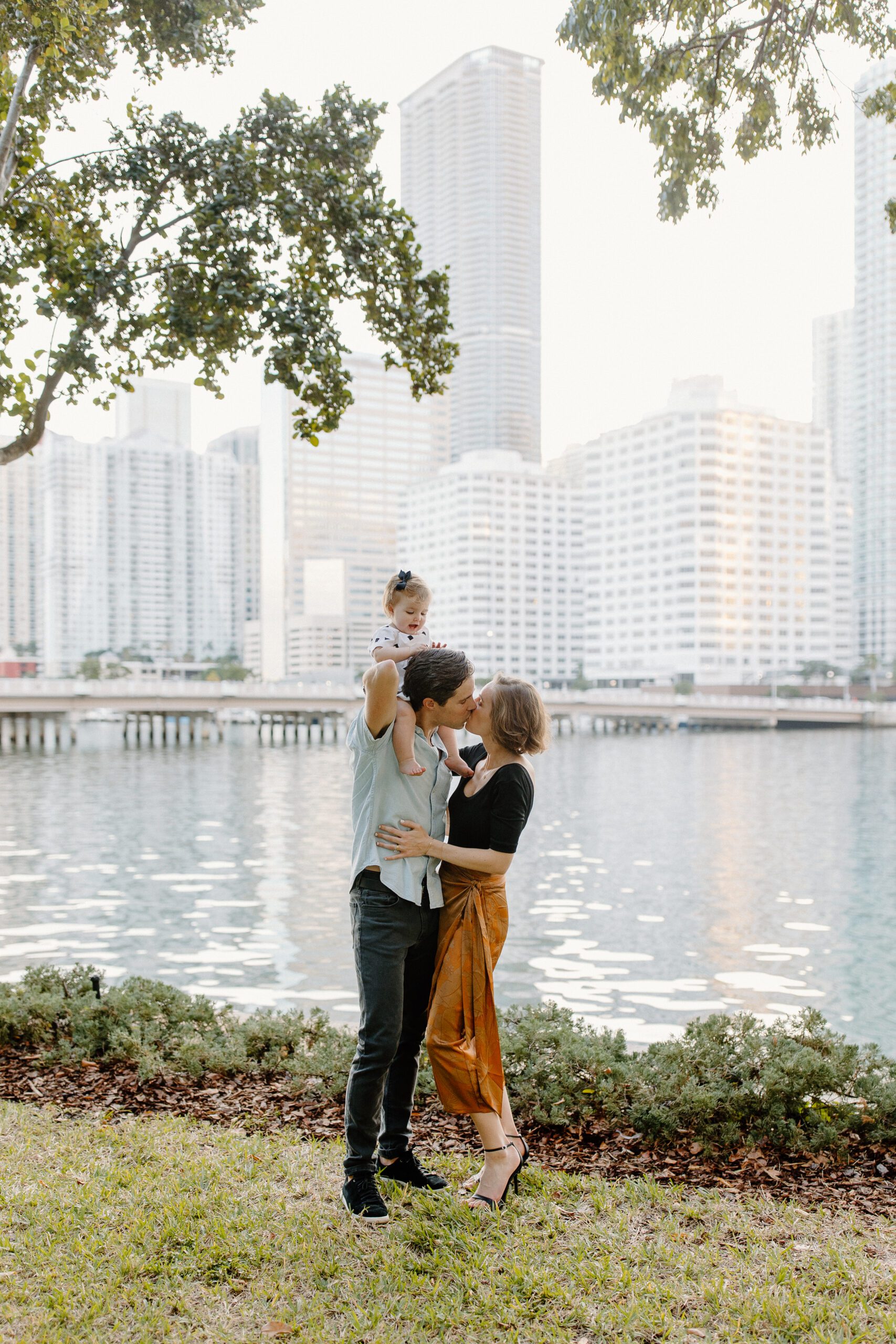 mom and dad with daughter in front of the ocean kissing at Brickel Key Park 